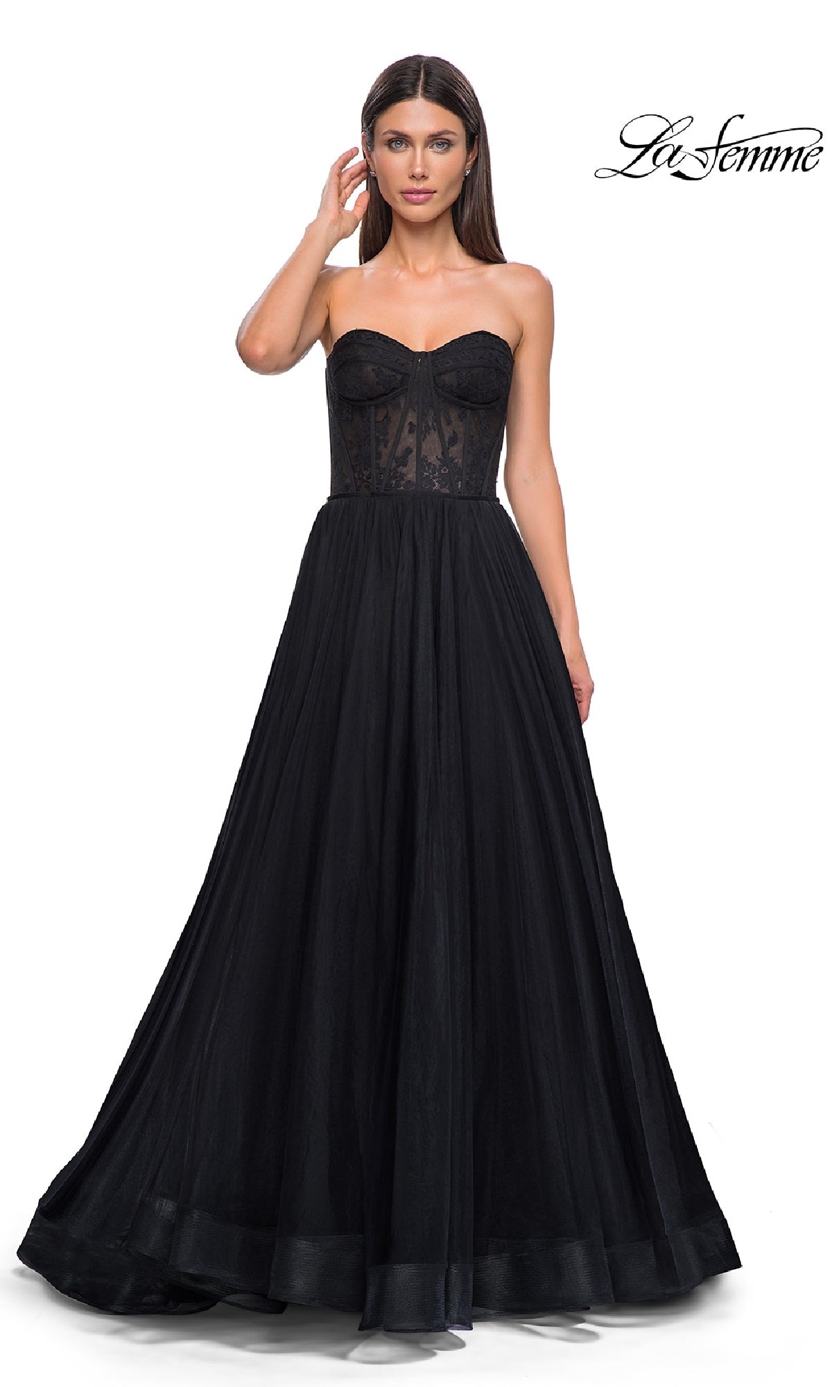 Woman wearing the Strapless Long Prom Ball Gown: La Femme 32579, featuring a fitted floral corset-style bodice and full black skirt, standing against a plain white background.